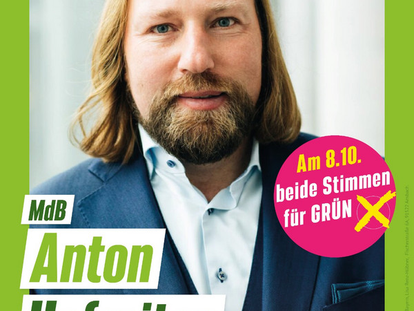 Plakat im grünen Rahmen mit Sonnenblume rechts oben, auf dem Toni Hofreiter den Betrachter direkt ansieht. Ein runderStörer rechts im Bild fordert dazu auf, bei der bayerischen Landtagswahl  am 08.10.2023 den Grünen beide Stimmen zu geben. Der Text unter Toni Hofreiters Bild kündigt  "MdL Anton Hofreiter vor Ort" am 21. Juli, 19:00 Uhr, Gasthaus zur Krone, Petersaurach" an 